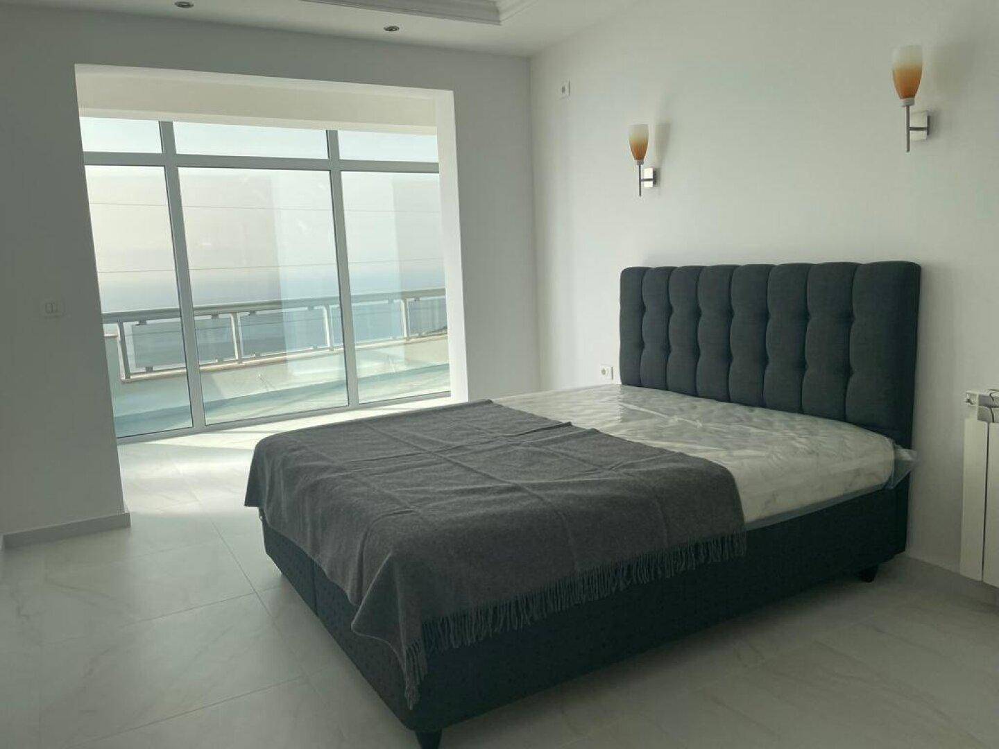 Schlafzimmer mit modernem Bett und großen Fenstern, die einen beeindruckenden Meerblick ermöglichen.