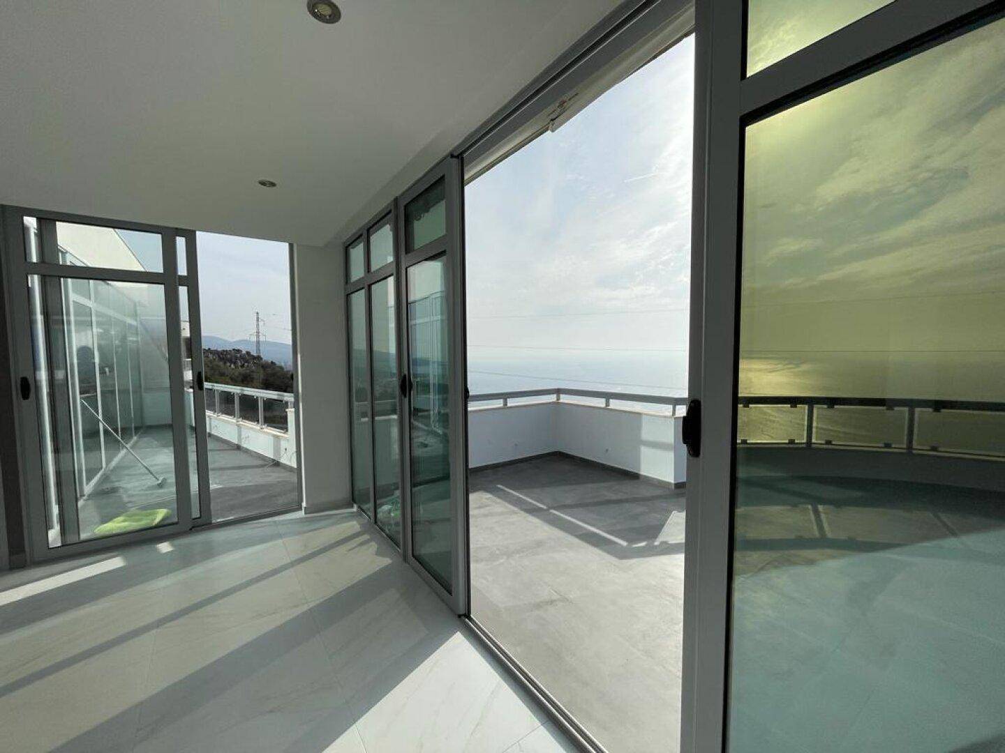 Lichtdurchfluteter Raum mit Schiebetüren, die zu einer großen Terrasse mit Meerblick führen.