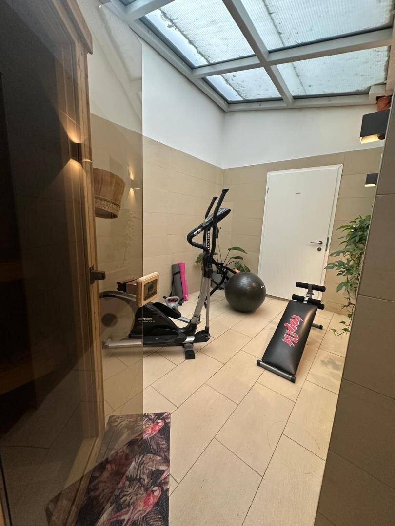 Fitnessbereich mit Trainingsgeräten und einer Sauna, beleuchtet durch ein großes Oberlicht.