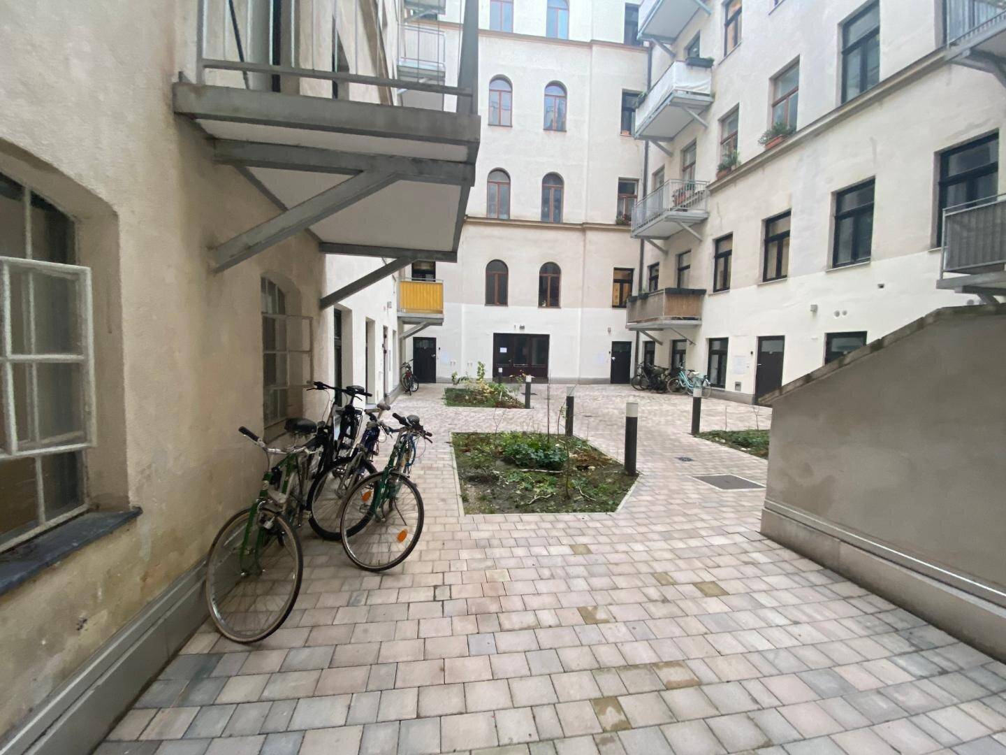 Innenhof eines Gebäudekomplexes mit gepflasterten Flächen, kleinen Grünbeeten und Fahrradstellplätzen.