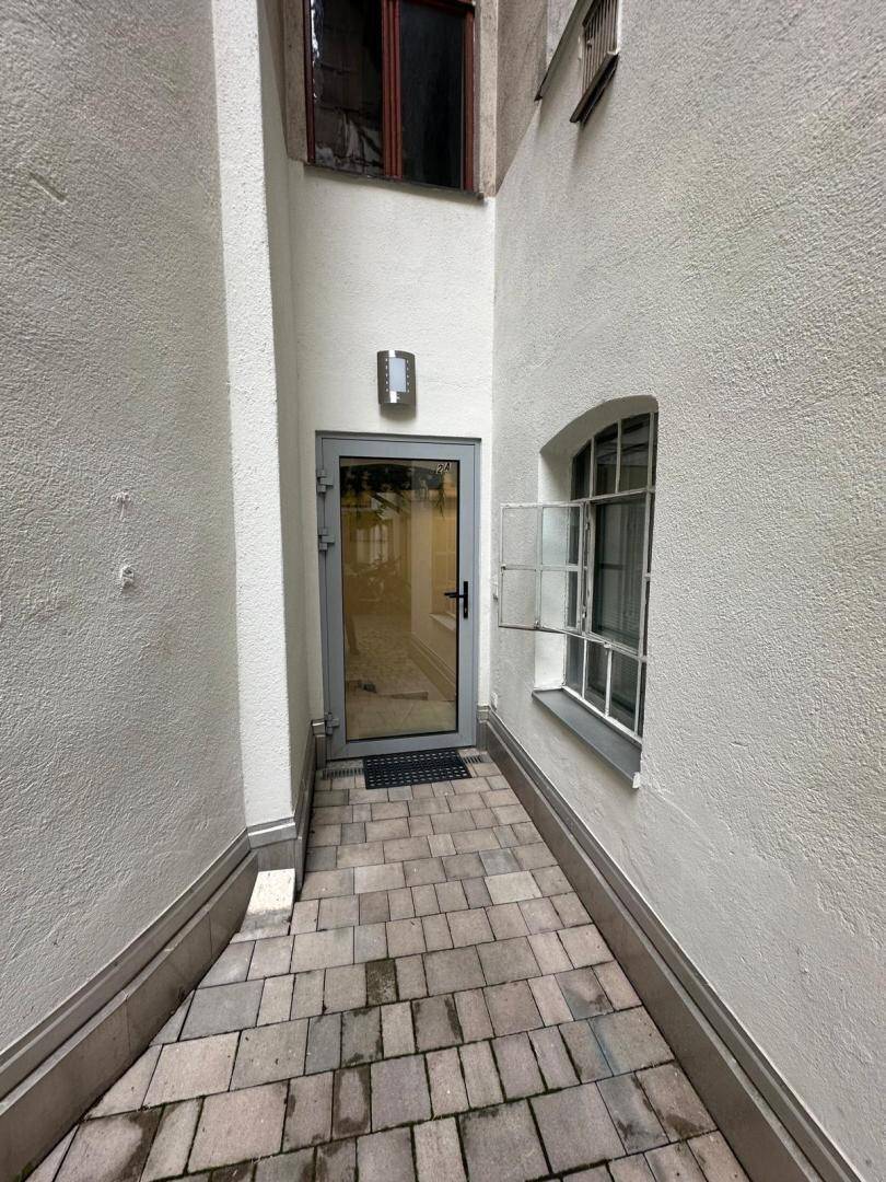 Schmaler gepflasterter Weg führt zu einem Eingangsbereich mit einer modernen Glastür.