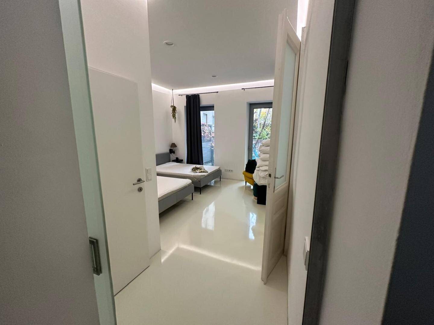 Helles Schlafzimmer mit zwei Einzelbetten und Zugang zu einem Außenbereich durch große Fenster.