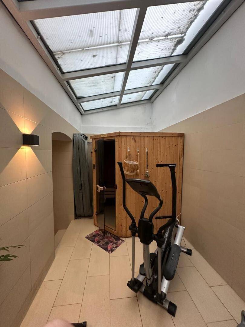 Geräumiger Wellnessbereich mit Sauna und Fitnessgeräten unter einem großen Glasdach.