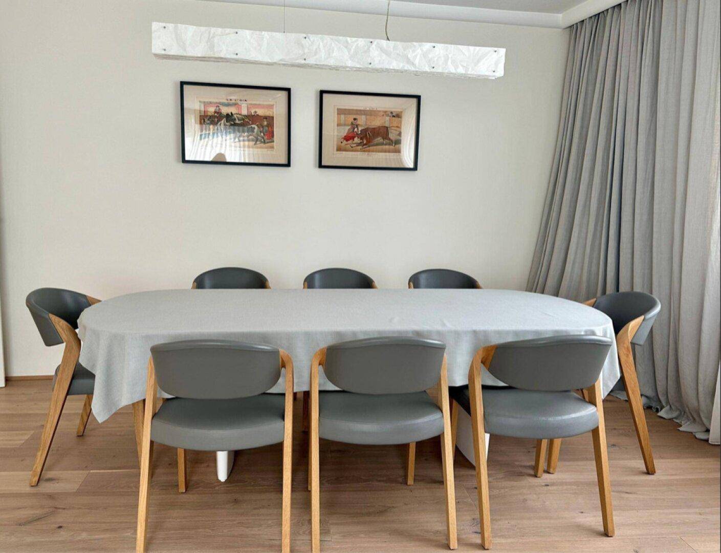 Heller Essbereich mit modernem Esstisch, bequemen Stühlen und Kunstwerken an der Wand.