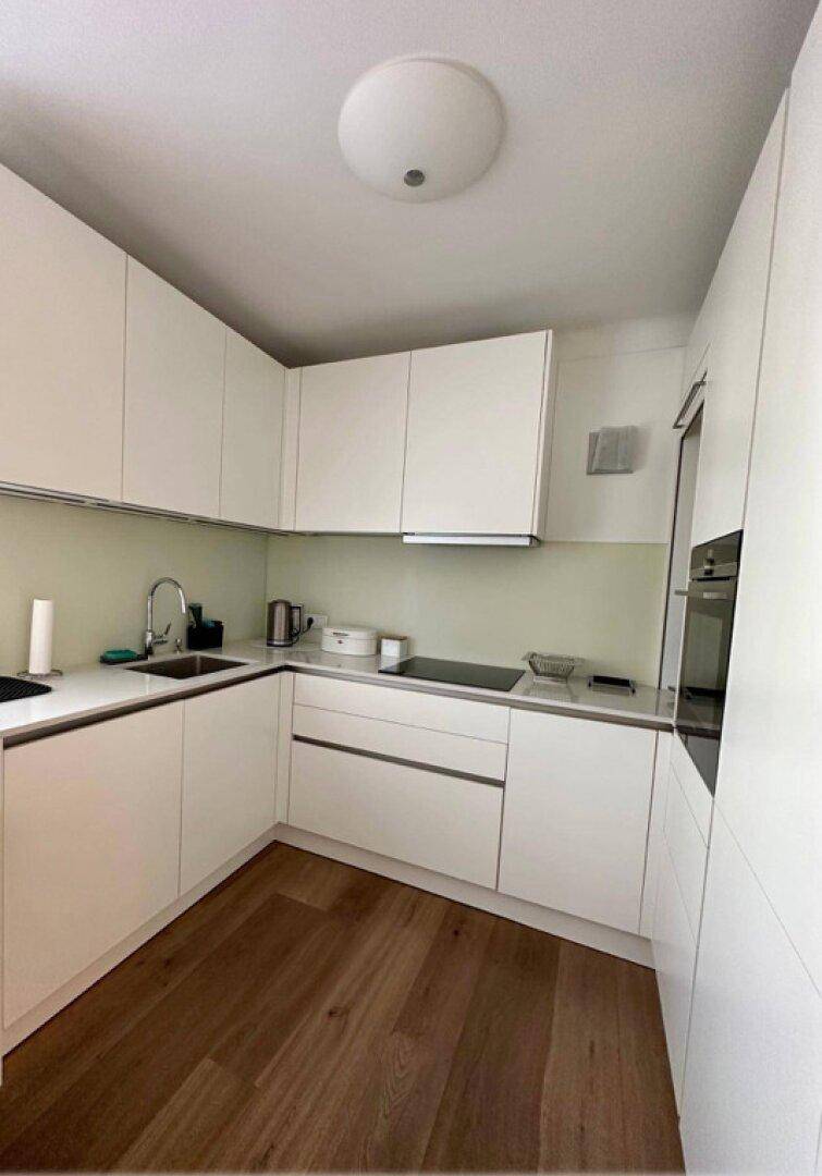 Moderne weiße Küche mit Einbaugeräten, Holzboden und minimalistischem Design.