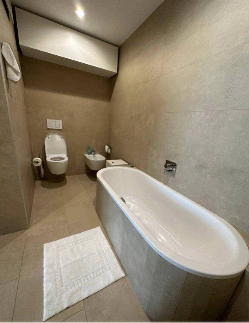 Geräumiges Badezimmer mit Badewanne, Toilette, Bidet und beigefarbenen Fliesen.