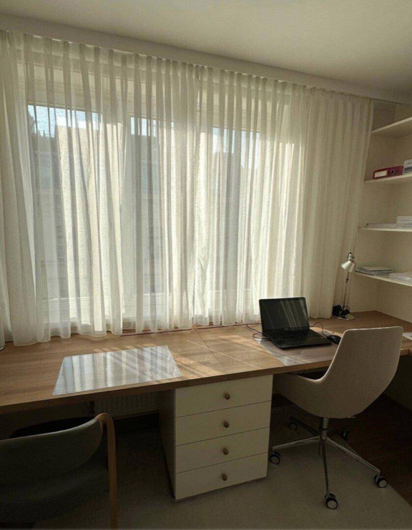Geräumiger Schreibtischbereich mit Laptop, Bürostuhl und viel natürlichem Licht.