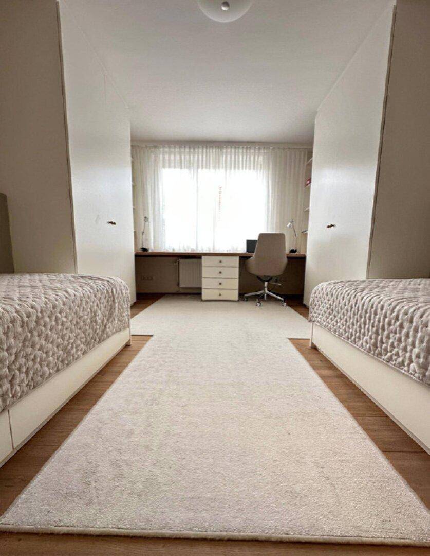 Helles Arbeitszimmer mit zwei Betten, großem Schreibtisch und viel Tageslicht.