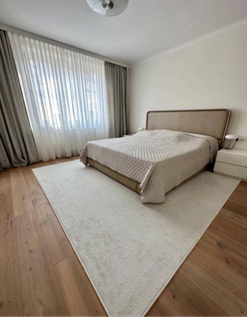 Schlafzimmer mit großem Bett, Holzboden und hellem Teppich unter dem Bett.