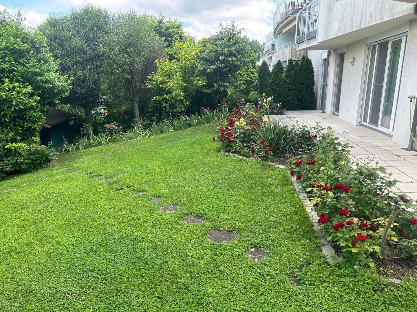 Gepflegter Garten mit Rasen, Blumenbeeten und einer gepflasterten Terrasse am Haus.