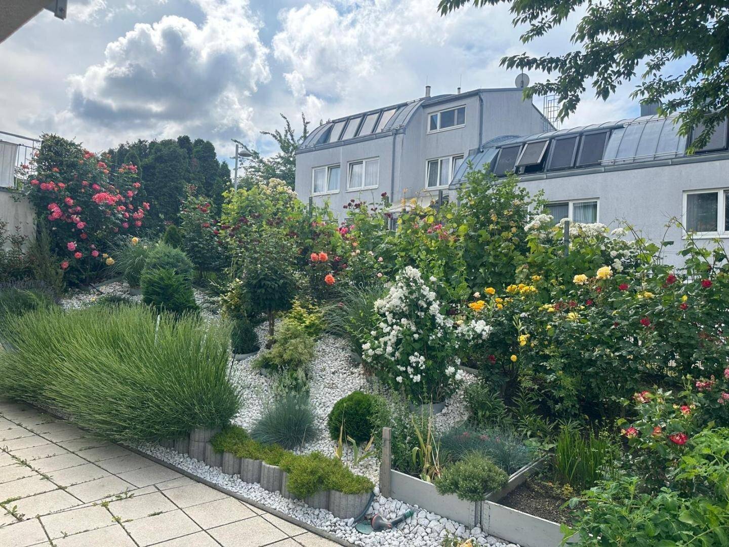 Gestufter Garten mit vielfältiger Bepflanzung, Ziersteinen und einem Wohngebäude.