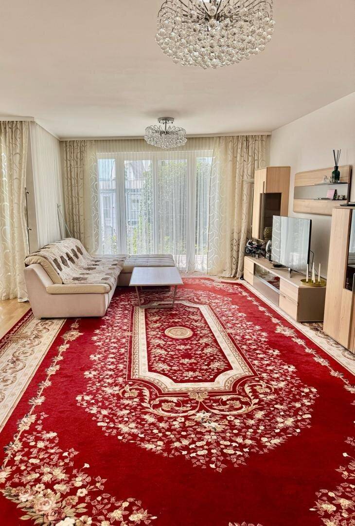 Gemütliches Wohnzimmer mit beigem Sofa, TV-Möbeln und einem opulenten roten Teppich.