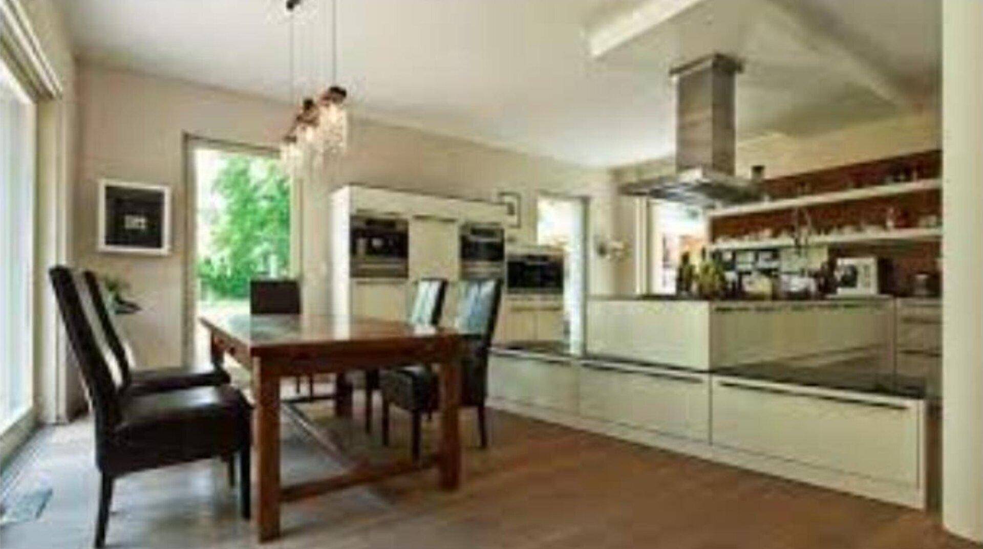 Heller Essbereich mit Holztisch und offener, moderner Küche im Hintergrund.