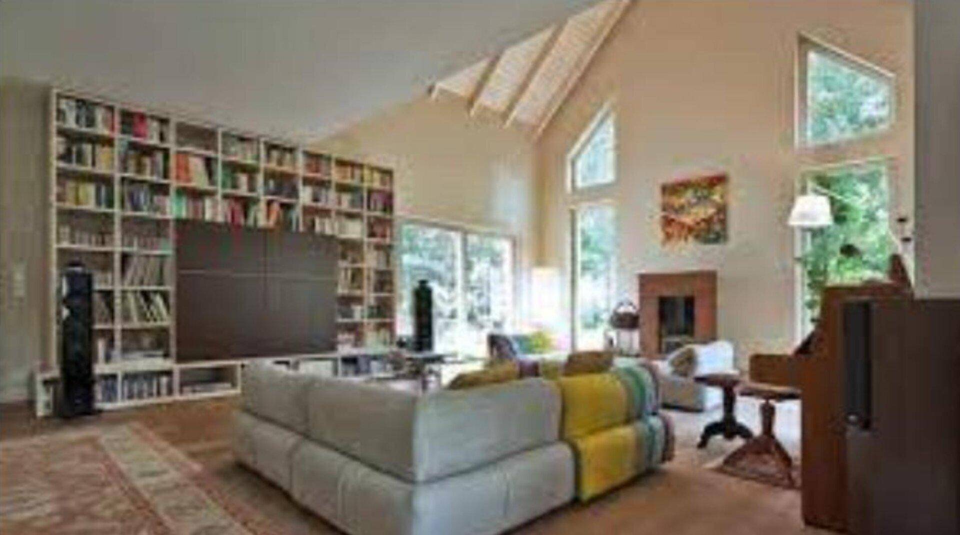 Geräumiges Wohnzimmer mit hoher Decke, Bücherregal, Kamin und großen Fenstern.