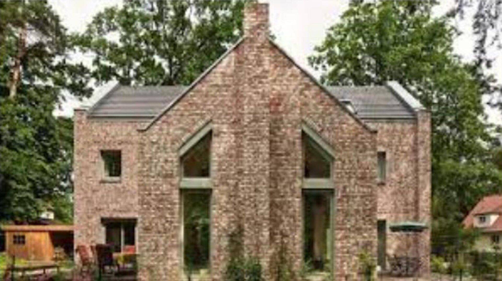 Moderne Backsteinfassade mit großen Fenstern und markanter Architektur, umgeben von Bäumen.