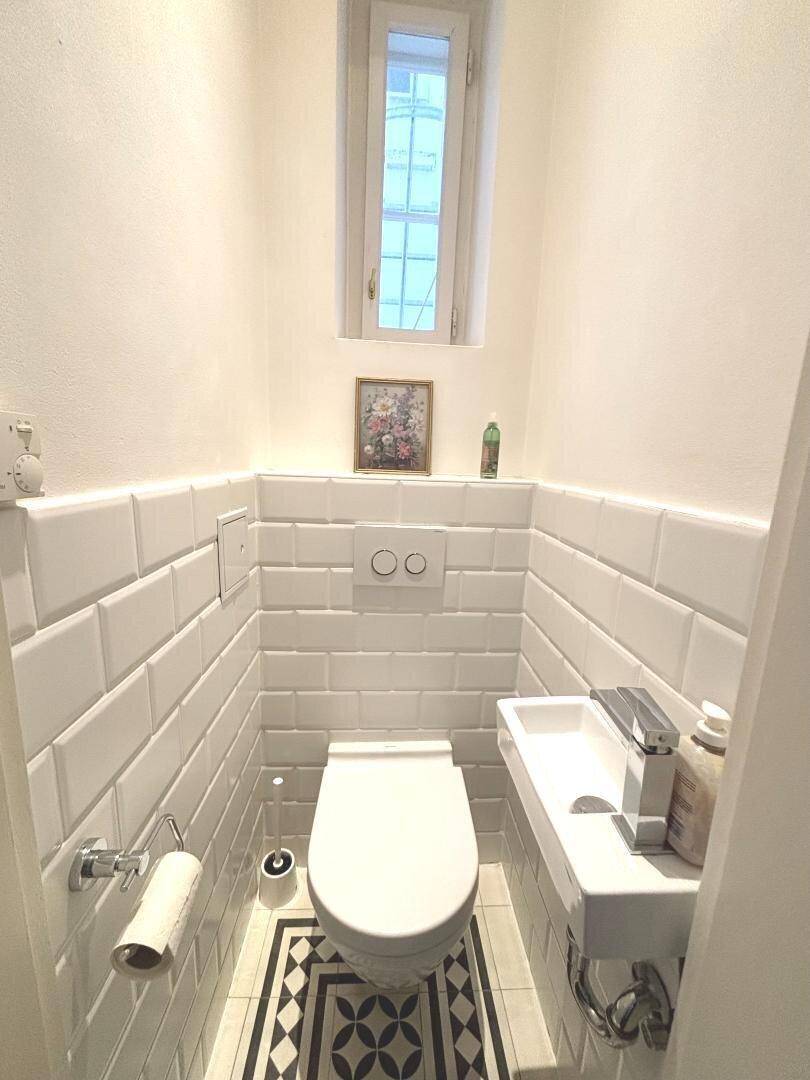 Gäste-WC mit wandhängendem WC, kleinem Waschbecken und Fenster.