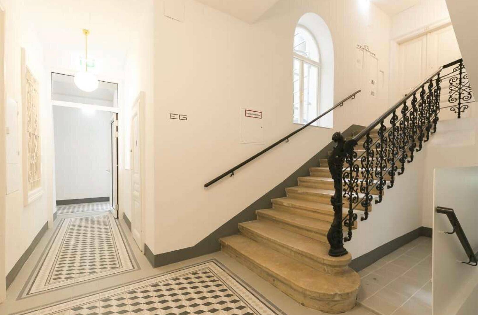 Treppenhaus mit kunstvollem Geländer, gemusterten Fliesen und hohen Decken.