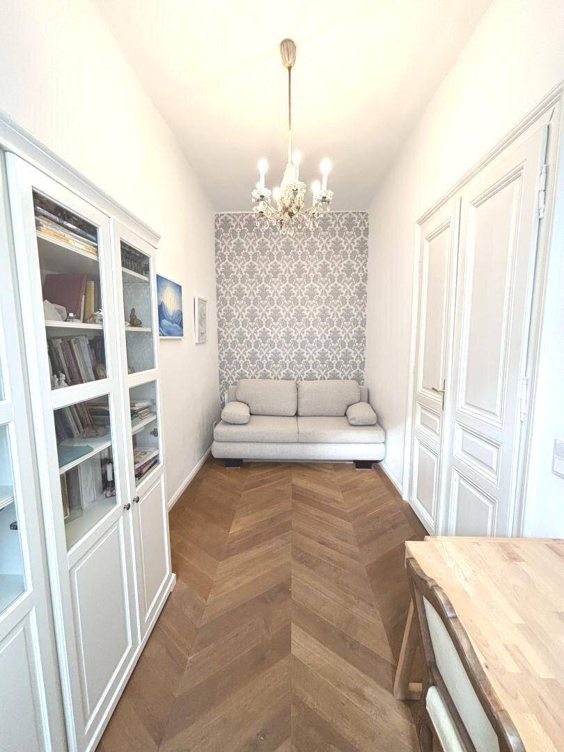 Heller Flur mit Sitzgelegenheit, Vitrine und gemusterter Akzentwand.