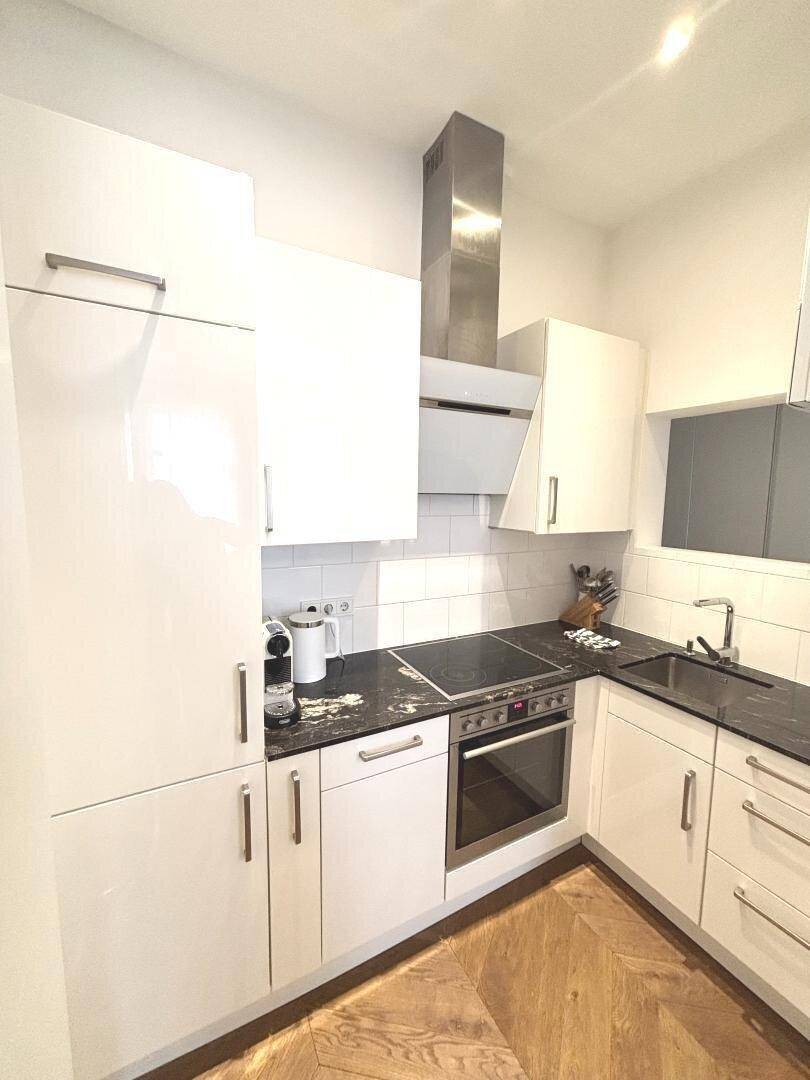 Moderne Einbauküche mit weißen Hochglanzfronten, Induktionskochfeld und Backofen.