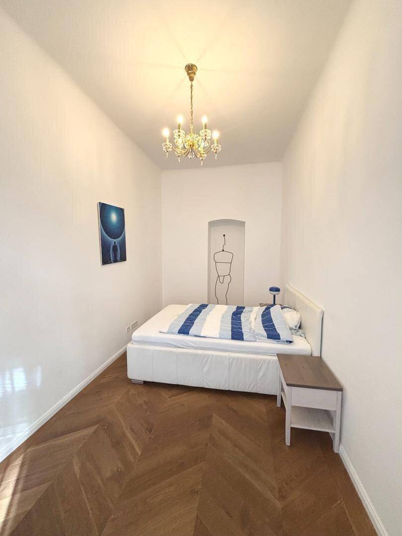 Schlafzimmer mit Bett, Beistelltisch und elegantem Kronleuchter.