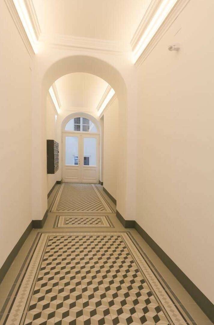 Langer Eingangsbereich mit gewölbter Decke, gemusterten Fliesen und Briefkästen.