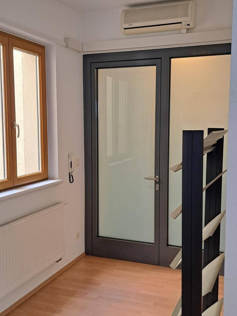 Heller Flur mit Laminatboden, Fenster, Heizkörper und einer modernen Glastür.