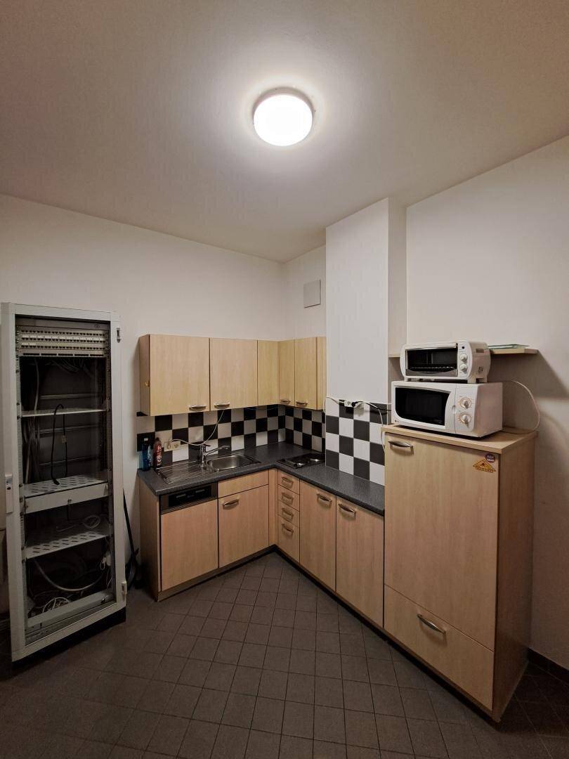 Kleine Küche mit hellen Holzschränken, kariertem Fliesenspiegel und Mikrowellen.