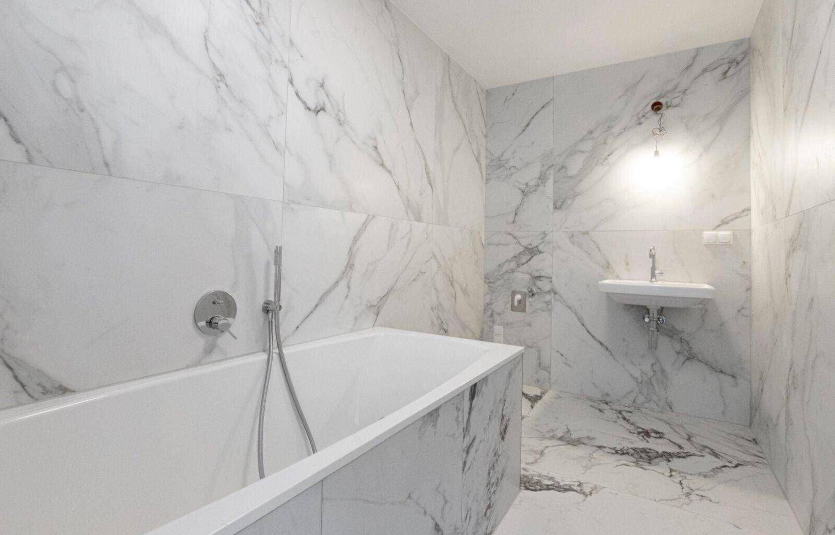 Modernes Badezimmer mit Marmoroptik-Fliesen, integrierter Badewanne und kleinem Waschbecken.