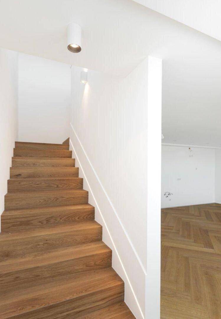 Moderne Holztreppe mit weißem Geländer und Blick auf den angrenzenden Fischgrätparkettboden.