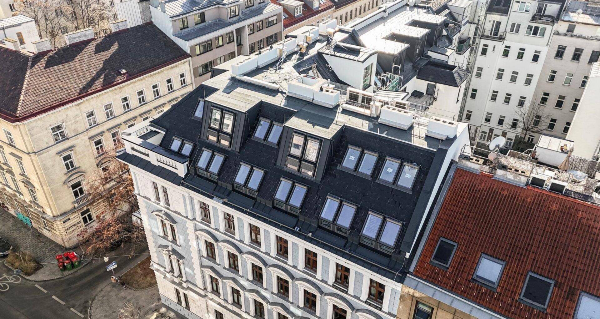Nahaufnahme eines Gebäudes von oben mit markantem Mansarddach und vielen Dachfenstern.