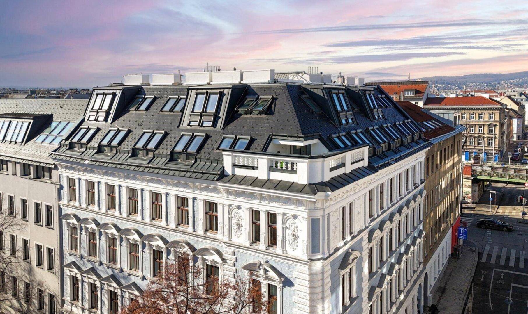 Luftaufnahme eines Stadtgebäudes mit Mansarddach und weitem Blick über die Dächer Wiens.