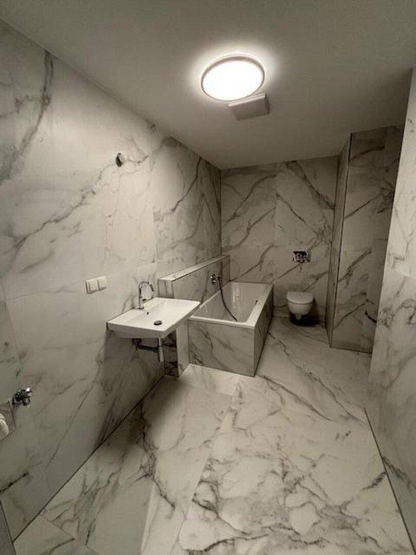 Elegantes Badezimmer mit Marmorfliesen, Badewanne, modernem Waschbecken und WC.