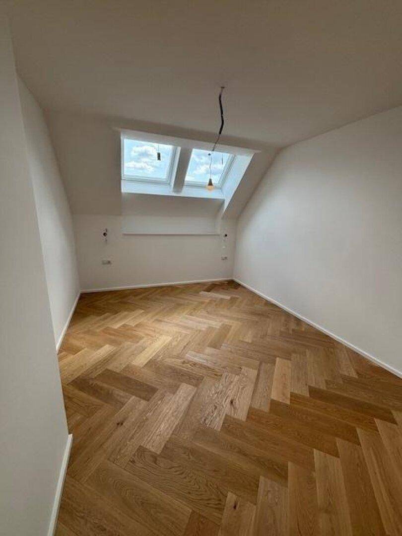 Helles Zimmer im Dachgeschoss mit Fischgrätparkett, Dachschrägen und zwei Dachfenstern.