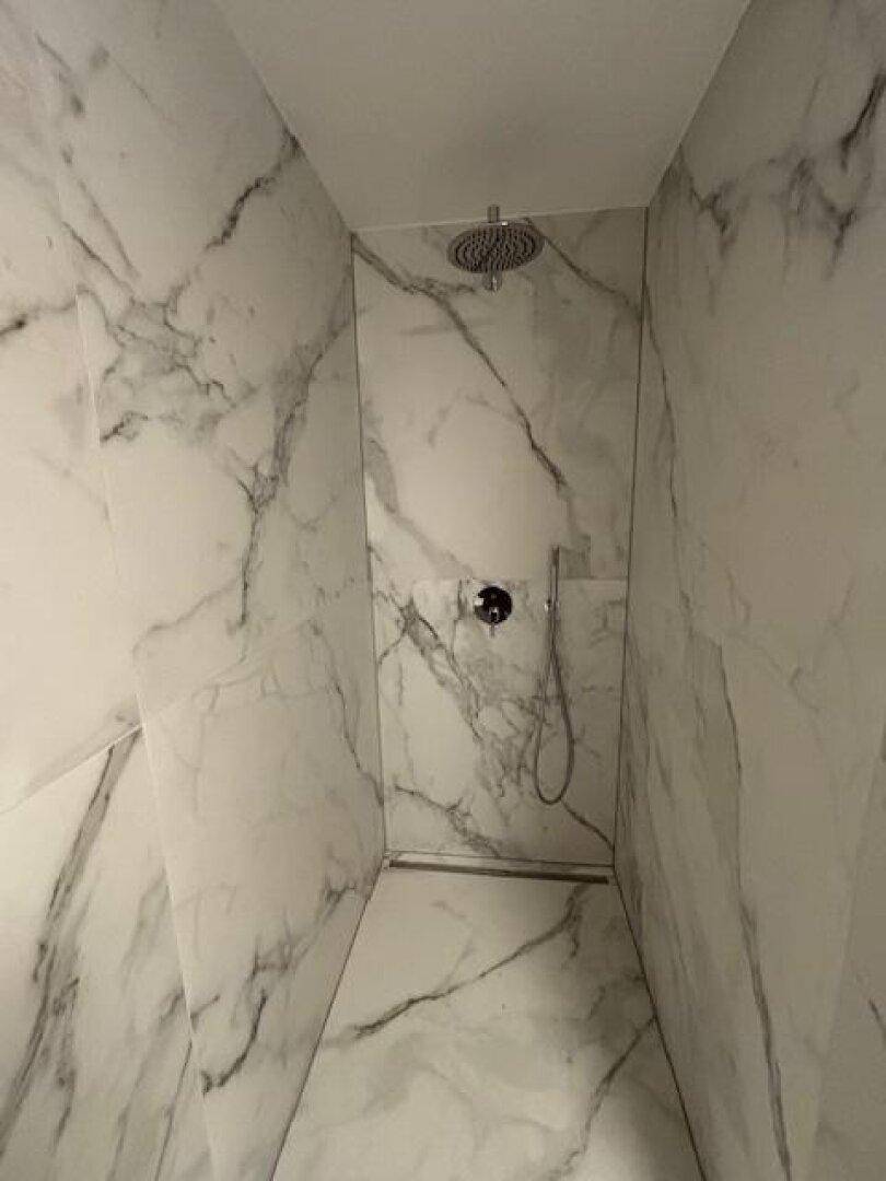 Moderne Duschkabine mit eleganten Marmorfliesen und einer luxuriösen Regendusche.