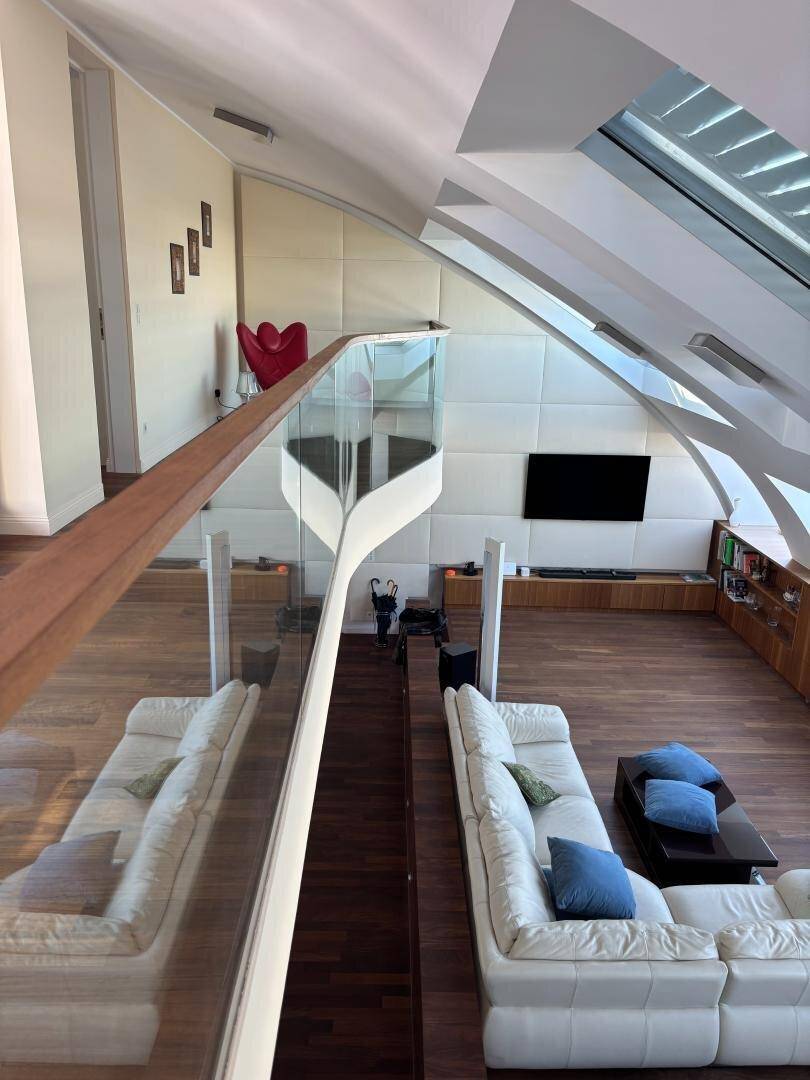 Blick von der Galerie in den offenen Wohnbereich mit Glasgeländer und modernen Dachfenstern.