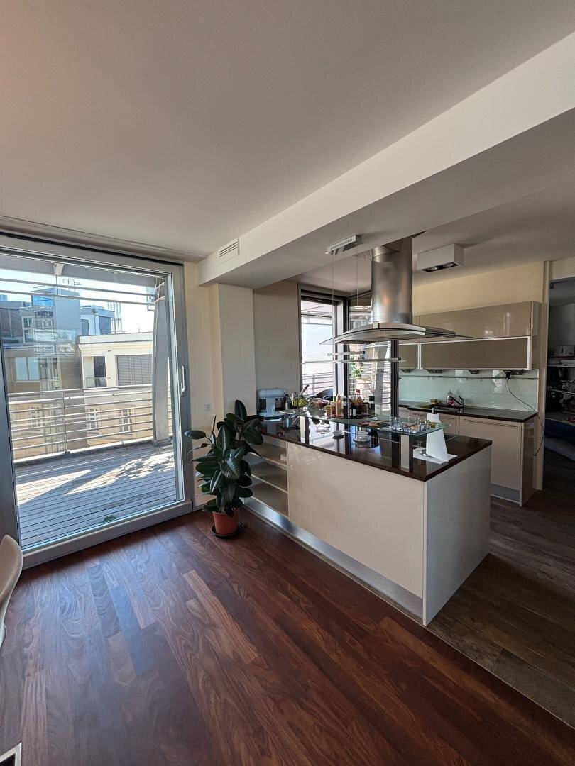 Moderne Küche mit Kochinsel, Dunstabzugshaube und direktem Zugang zu einer sonnigen Terrasse.