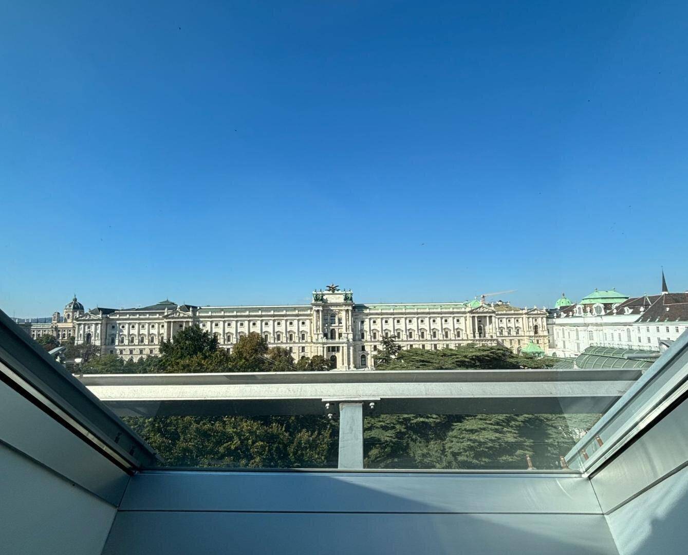 Panoramablick aus einem Dachfenster auf ein historisches Gebäude unter blauem Himmel.