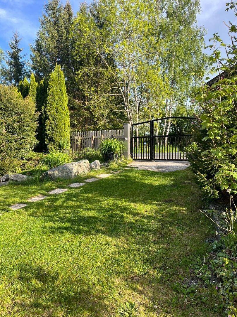 Grüner Gartenbereich mit Steinplattenweg und einem schwarzen Metalltor, umgeben von Bäumen und Sträuchern.