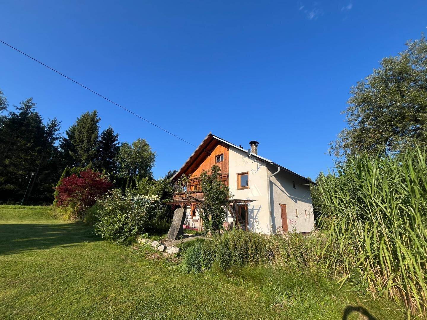 Seitenansicht des Hauses mit grünem Rasen und üppiger Vegetation unter blauem Himmel.