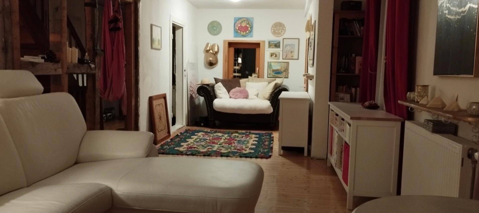 Gemütliches Wohnzimmer mit hellem Sofa, Teppich und traditioneller Dekoration, die eine warme Atmosphäre schafft.
