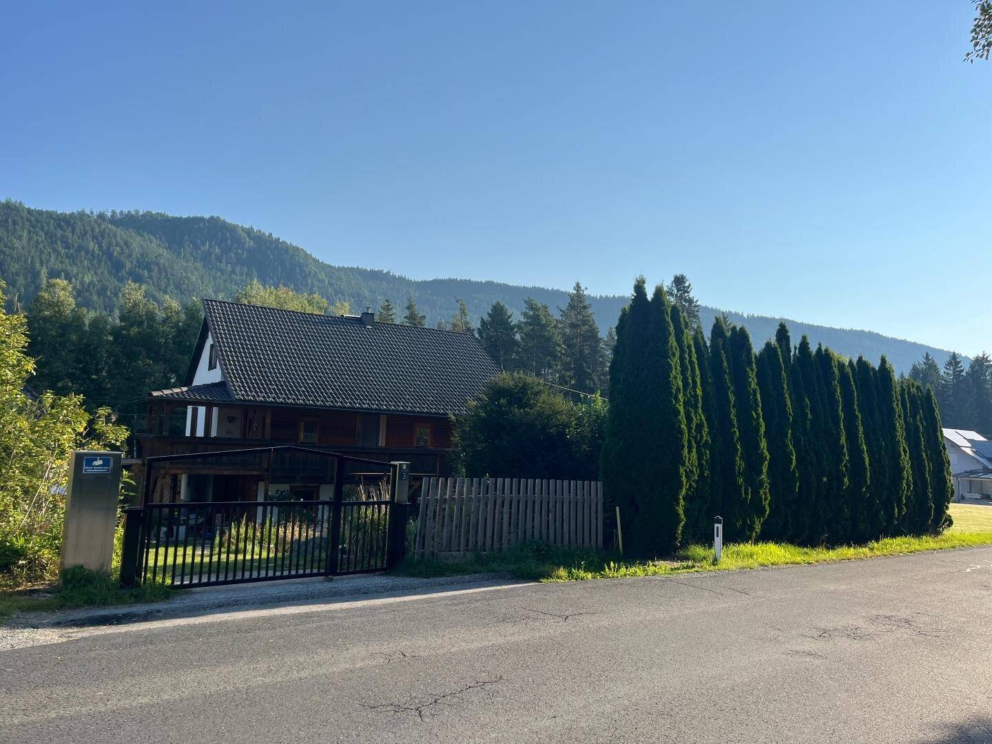 Ansicht des Hauses von der Straße mit Eingangstor und einer Reihe hoher Koniferen als Hecke.