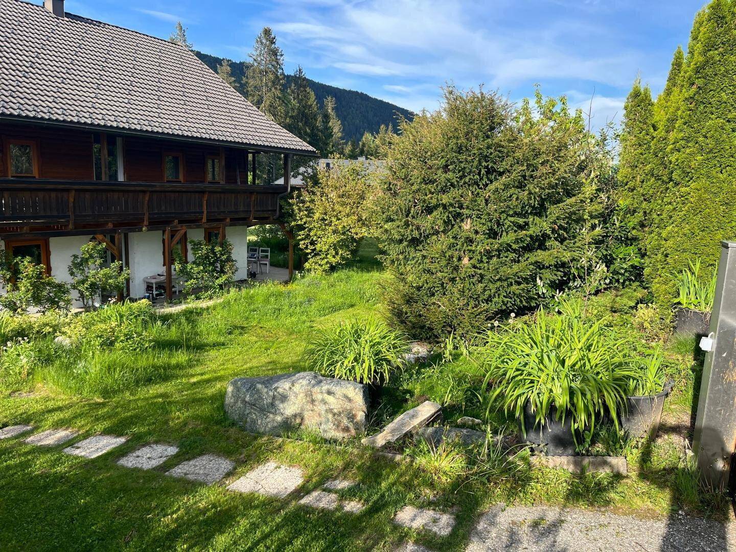 Gepflegter Gartenbereich mit großen Steinen, grünen Pflanzen und einem Weg aus Trittplatten.