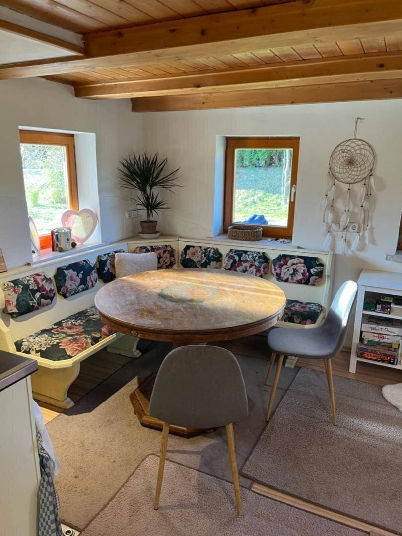 Gemütlicher Essbereich mit Holztisch, Eckbank und floralen Kissen unter einer Holzdecke.