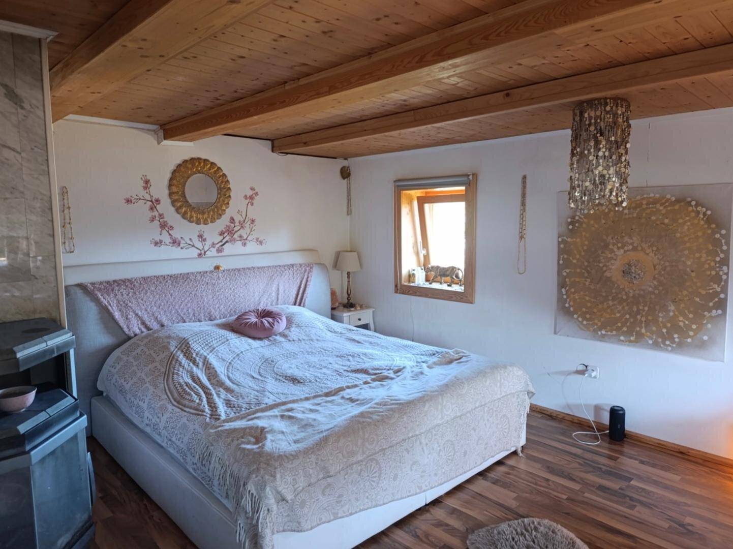 Schlafzimmer mit Holzbalkendecke, großem Bett und einem Kaminofen, der eine gemütliche Atmosphäre schafft.
