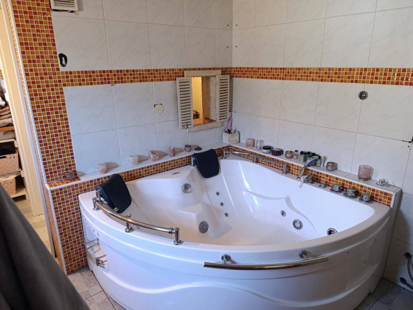 Badezimmer mit einer großen Eck-Whirlpool-Badewanne und farbigen Fliesen an den Wänden.