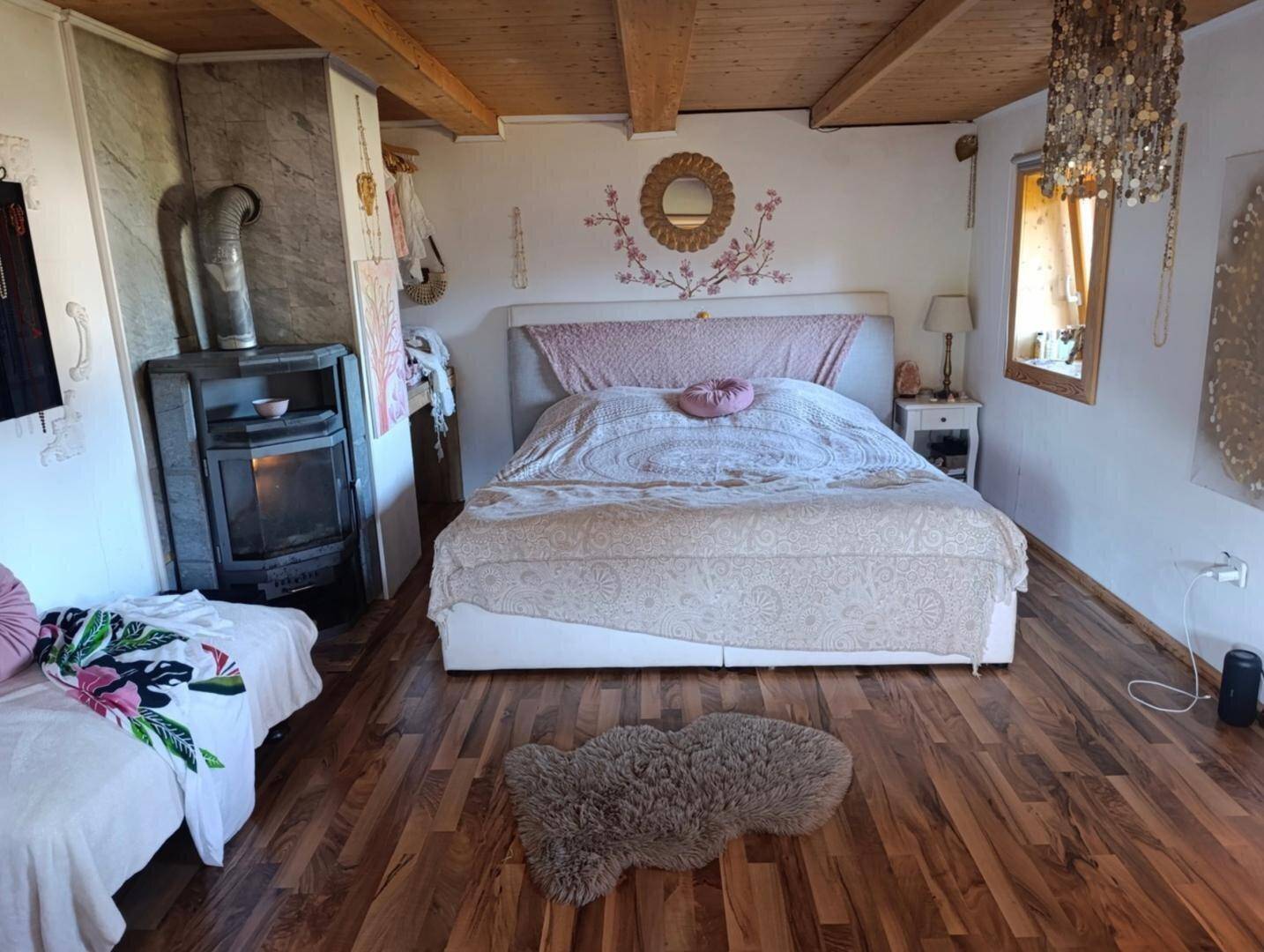 Gemütliches Schlafzimmer mit Holzbalkendecke, großem Bett und Kaminofen, dekoriert mit Wandkunst.
