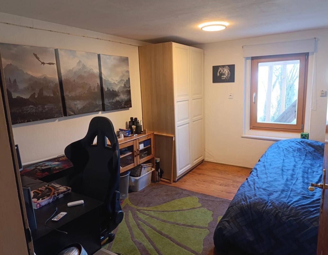 Schlafzimmer mit Holzboden, einem Bett und einem Schreibtisch mit Gaming-Stuhl, dekoriert mit Wandbildern.