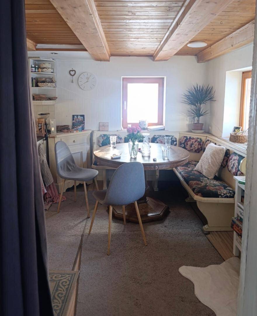 Gemütlicher Essbereich mit Holzbalkendecke, einem runden Esstisch und einer Eckbank mit floralen Polstern.