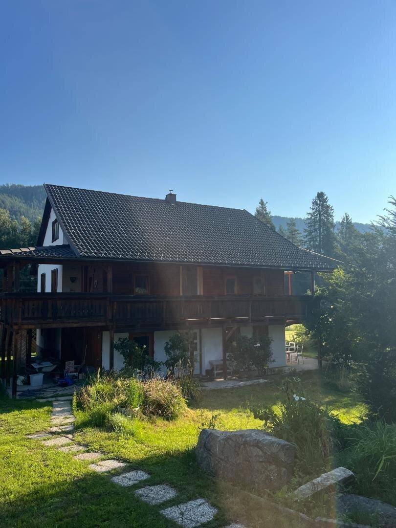 Rückansicht des Hauses mit mehreren Holzterrassen, Ziegeldach und Steinweg im Garten.