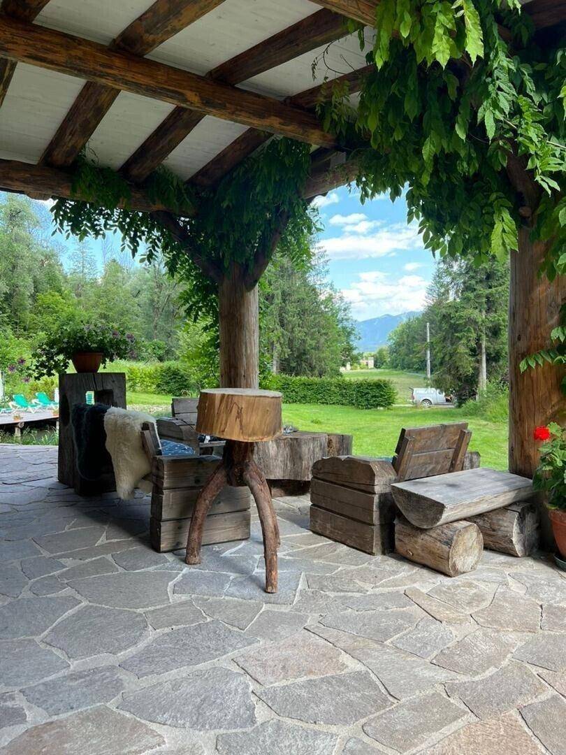 Überdachte Terrasse mit rustikalen Holzmöbeln und Steinboden, umgeben von üppigem Grün.